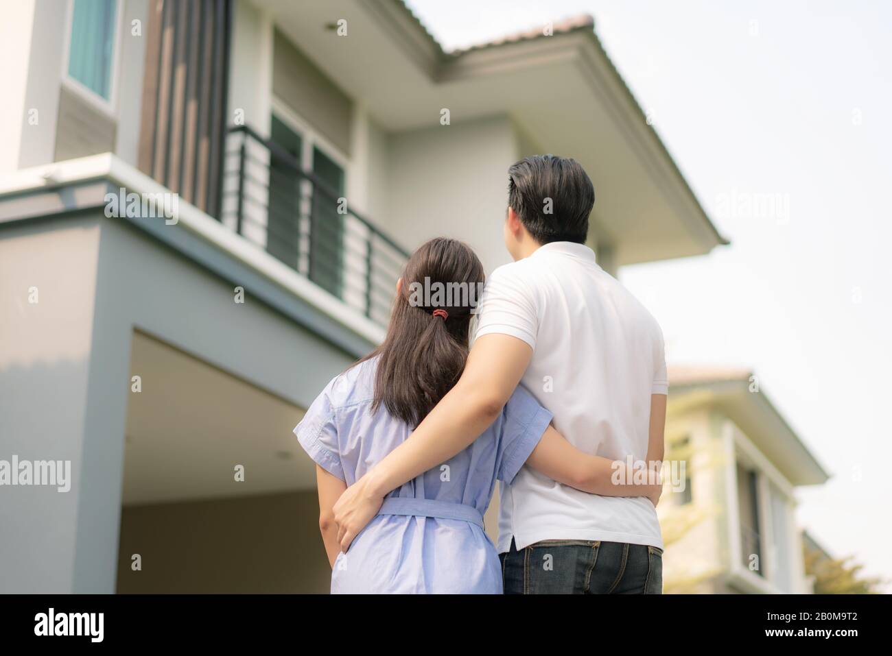 Hinteres Porträt des jungen asiatischen Paares, das zusammen steht und umarmt und vor ihrem neuen Haus glücklich aussieht, um neues Leben zu beginnen. Familie, Alter, Zuhause, echt Stockfoto