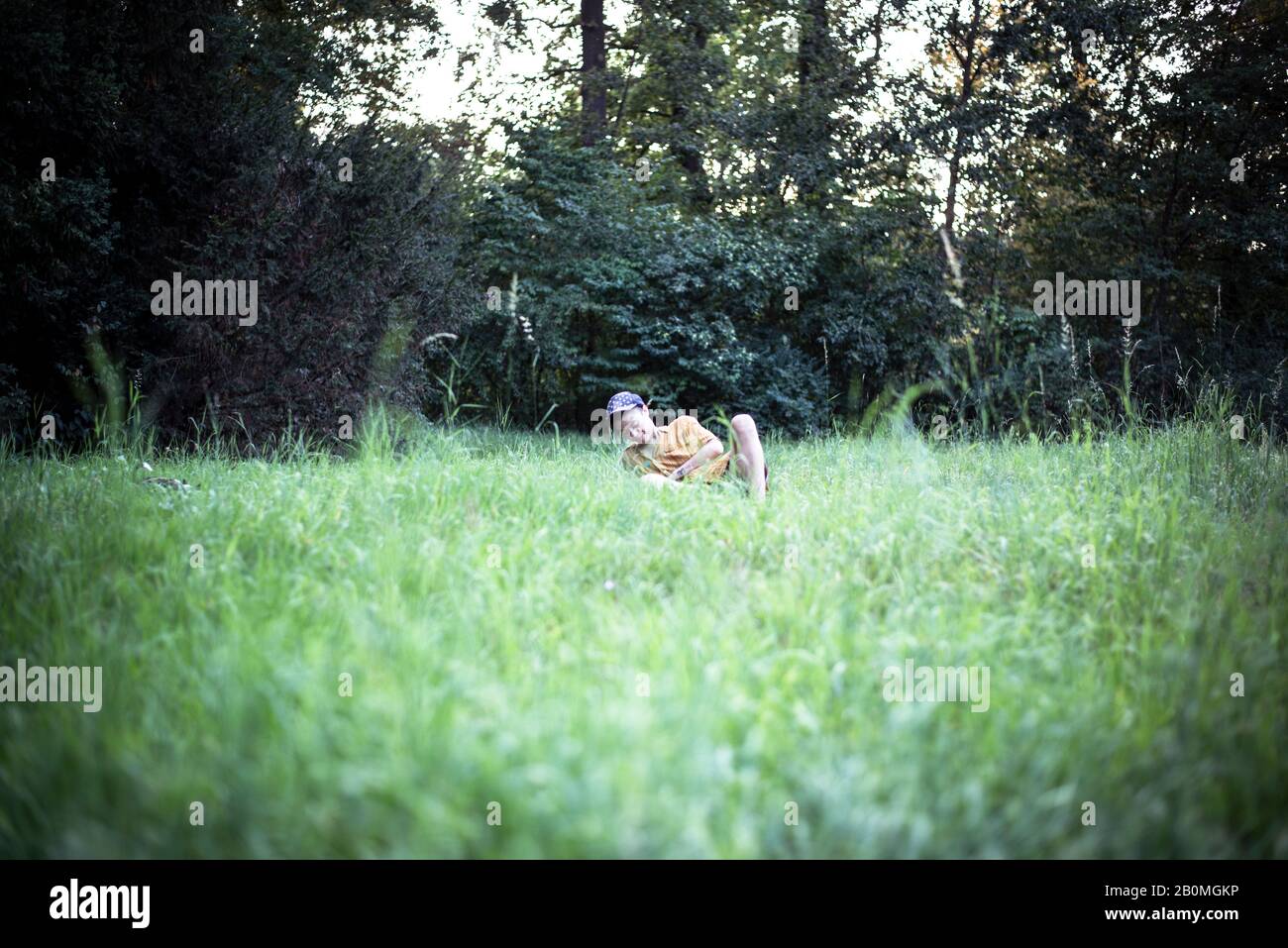 Person mit Mütze sitzt glücklich im Grasfeld während des Sommer-Picknicks Stockfoto