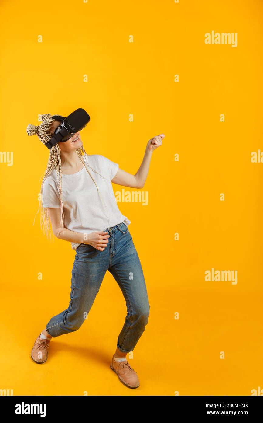 Frau spielt virtuelle Gitarre im Virtual Reality Headset auf Gelb. Stockfoto