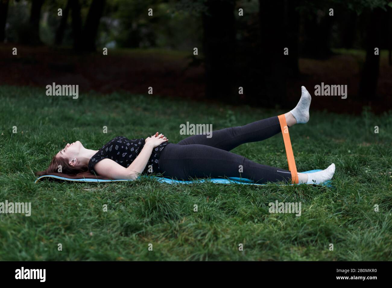 Mädchen dehnt sich mit einem Gummiband auf einer Yogamatte im Park Stockfoto