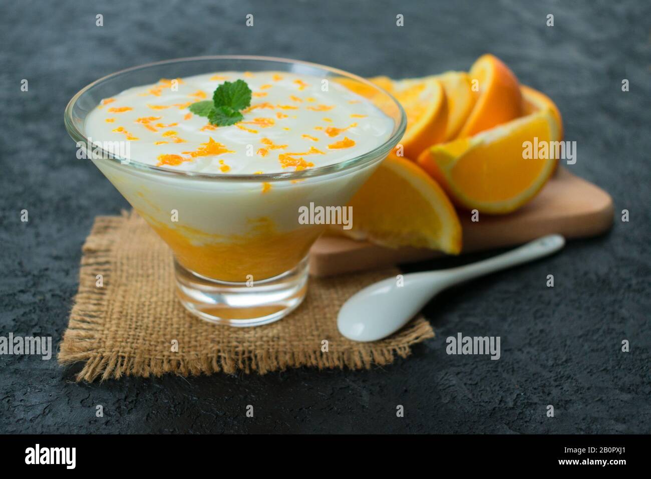 Erfrischendes Joghurt Dessert mit orangefarbenem Smoothie auf schwarzem Hintergrund. Stockfoto