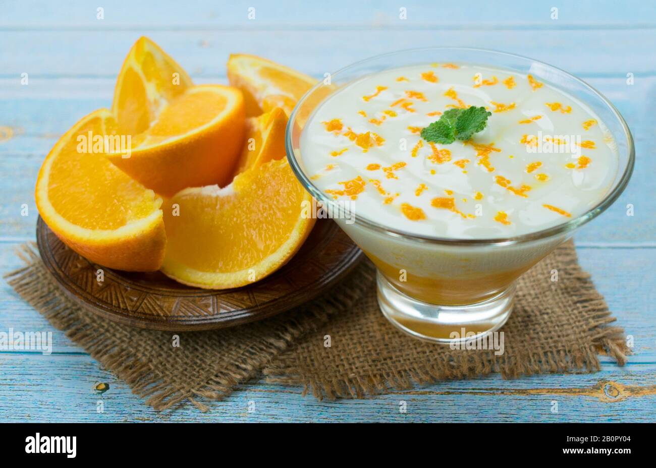 Gesunder Joghurt mit orangefarbenem Smoothie auf blauem Holzhintergrund. Konzept der gesunden Desserts. Stockfoto