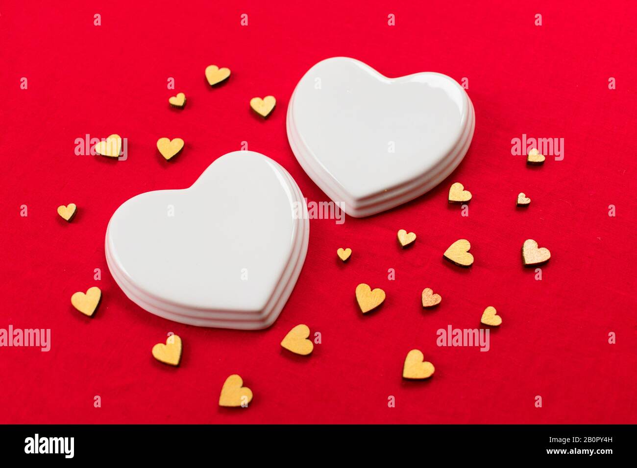 Zwei weiße Porzellanherzen und viele kleine Herzen auf rotem Hintergrund. Stockfoto