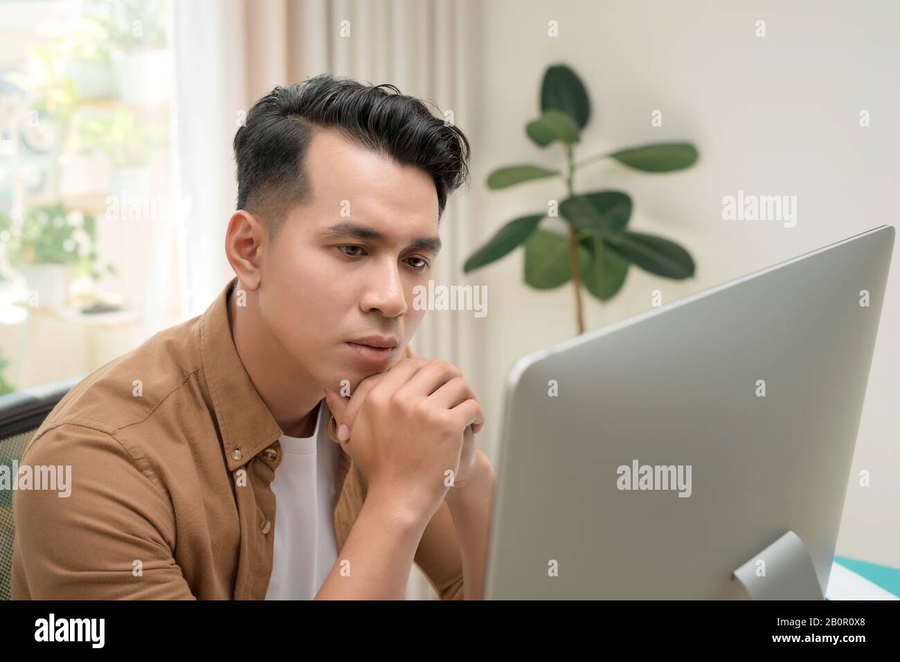 Asiatischer Mann, 25 bis 35 Jahre am Schreibtisch und lächelnd glücklich. Er überwacht den Verkauf auf dem Computerbildschirm. Stockfoto