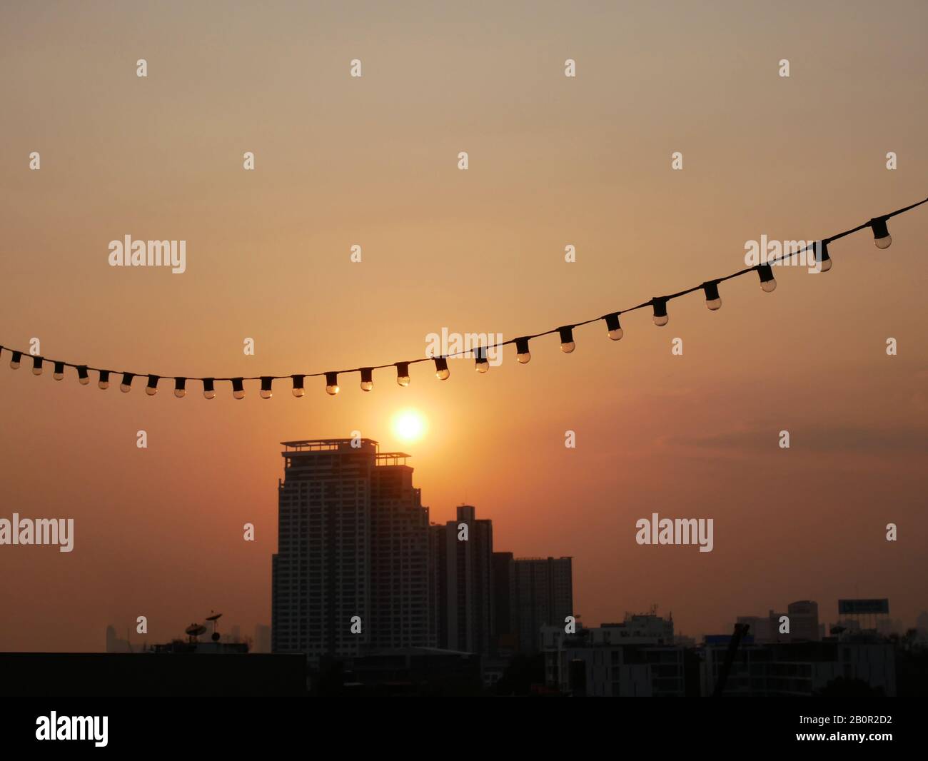 Bangkok City Blick vom Dachgebäude in der Dämmerung vor Sonnenuntergang mit Glühbirne Elektrodraht im Vordergrund hängen. Bild des Sonnenuntergangs in der Stadt Stockfoto