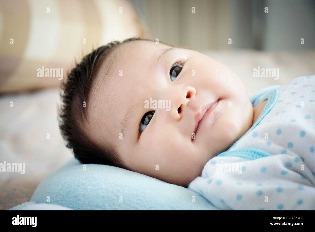 Asiatisches Babyportrait. Süßes asiatisches Mädchen öffnet die Augen auf dem komfortablen Bett, das Eltern am Tag mit einem kleinen Lächeln sucht. Fröhliches Kinderkonzept. Stockfoto
