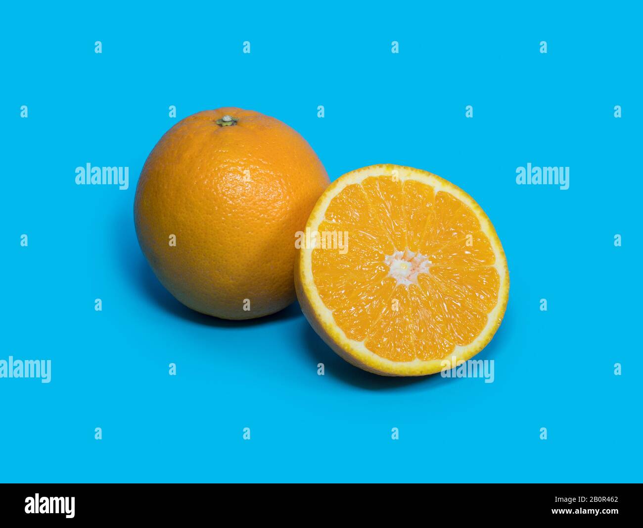 Frisches Orange mit halb Orange und Schatten isoliert auf blauem Hintergrund. Orangefarbener Fruchthintergrund Stockfoto