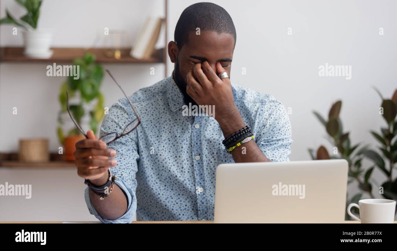 Der müde afroamerikanische Geschäftsmann, der Brille abnimmt, erschöpfte Angestellte, die Nasenbrücke massiert und nach langer Computerarbeit unter Augenbelastung leidet, F. Stockfoto