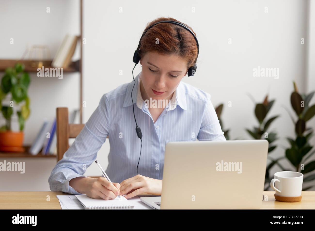 Fokussierte Frau in Kopfhörern mit Laptop, Notizen schreiben, Webinar zum Ansehen von Mitarbeitern, Schulung von Mitarbeitern, Sprache für Fernunterricht, E-Learning-Konzept, mA Stockfoto