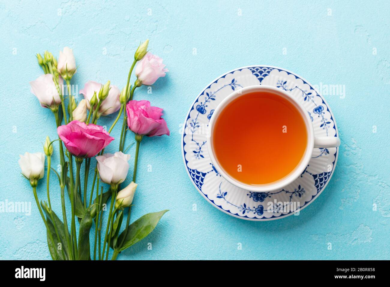 Tasse Tee mit pinkfarbenen Blumen, Eustom auf blauem Hintergrund. Draufsicht. Stockfoto