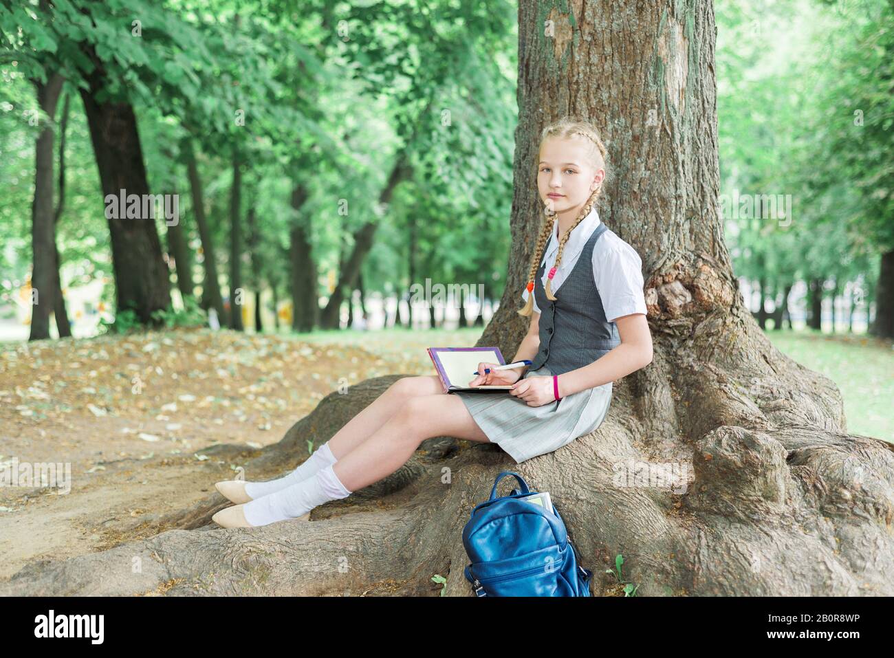 Schulmädchen unterrichtet Hausaufgaben im Park in der Nähe eines großen Baumes. Tutorial Stockfoto