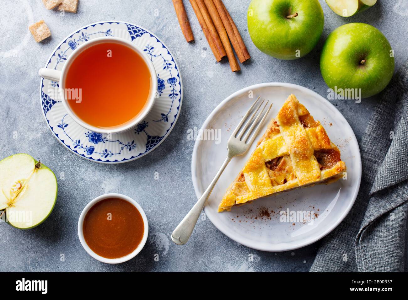 Apfelkuchen auf einem weißen Teller und einer Tasse Tee. Grauer Hintergrund. Draufsicht. Stockfoto