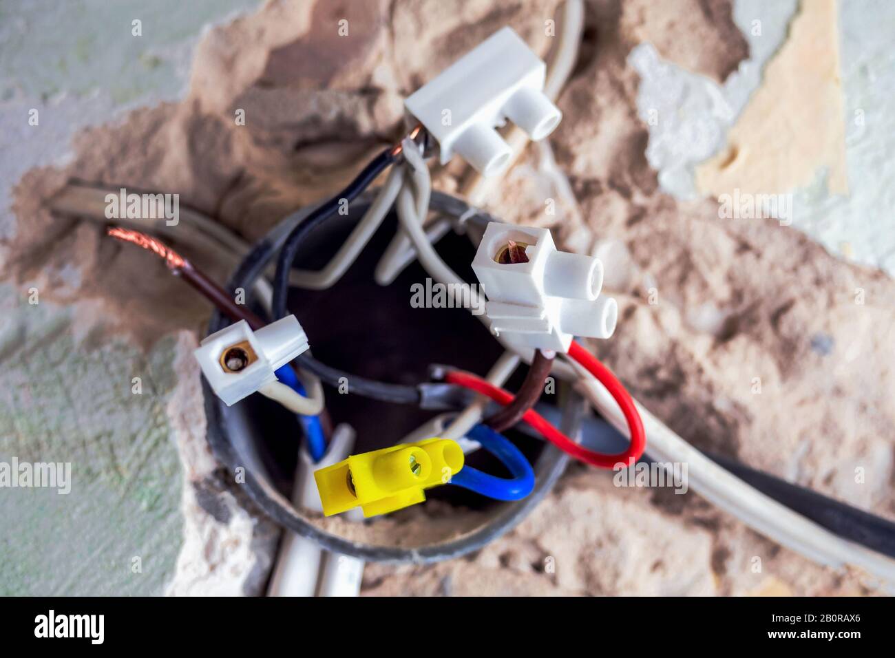 Reparatur- und Kabelinstallation. Elektrokasten mit aussteckenden Drähten in der alten Wand, die nicht mit einer Kappe bedeckt sind. Die elektrische Installation funktioniert. Selektiver Fokus Stockfoto