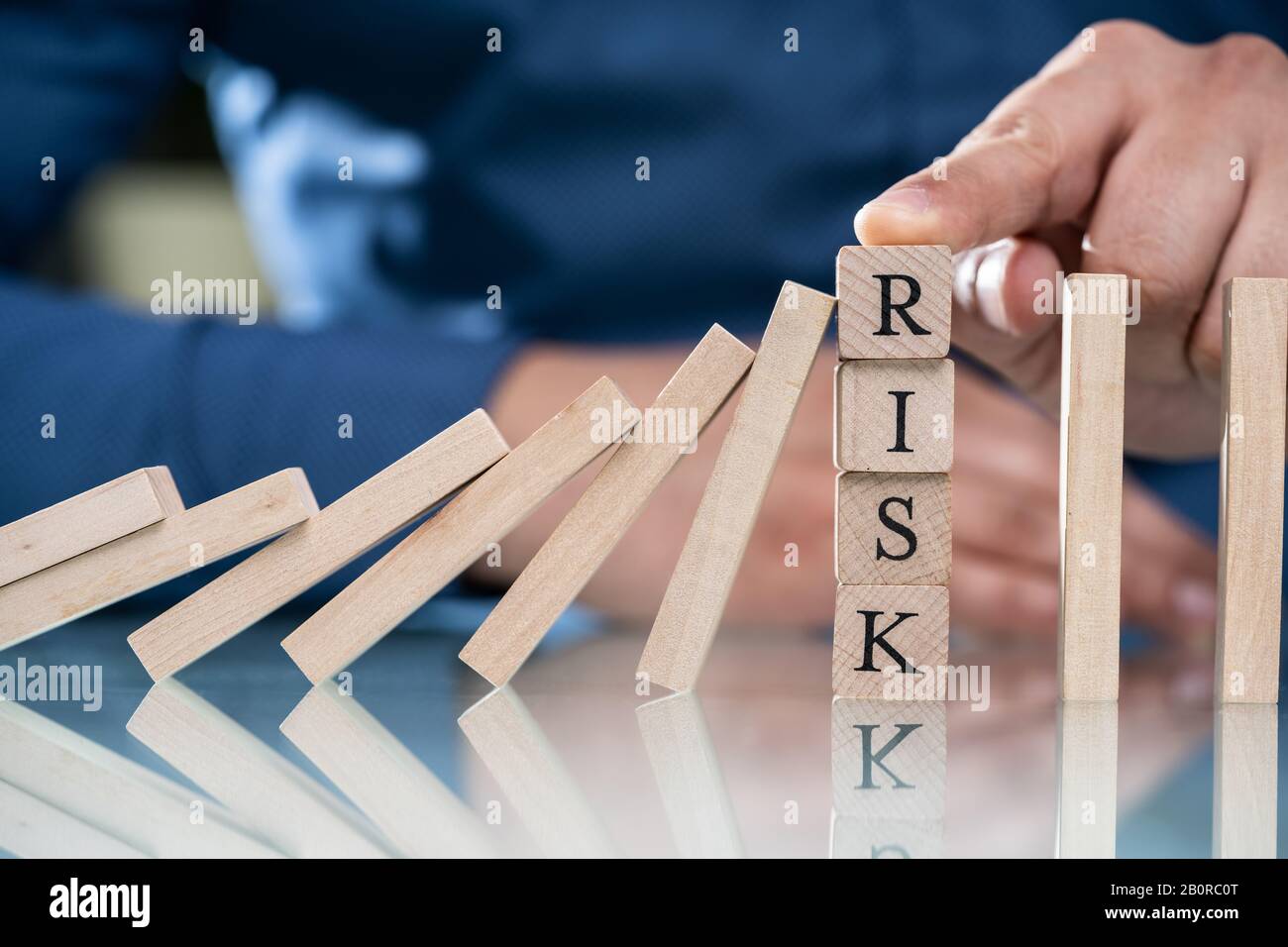 Der Finger von Geschäftsleuten Über Dem Risiko, dass Holzblöcke Dominoes Davon Abbringen, Auf den Schreibtisch Zu Fallen Stockfoto