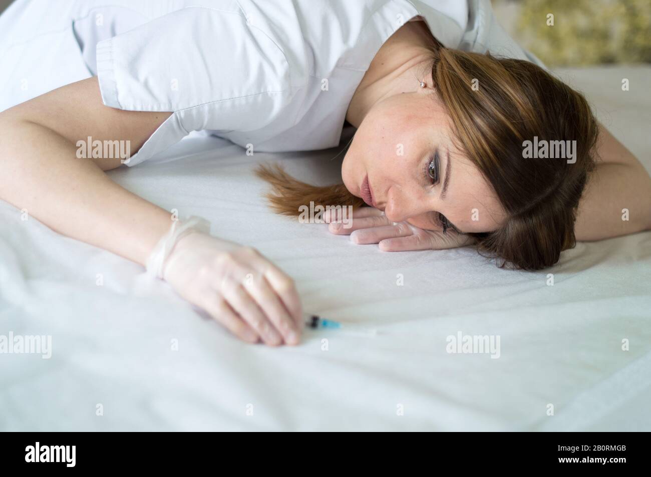 Frau Doktor im Krankenhaus müde, mit Spritze und chirurgischen Handschuhen liegend Stockfoto