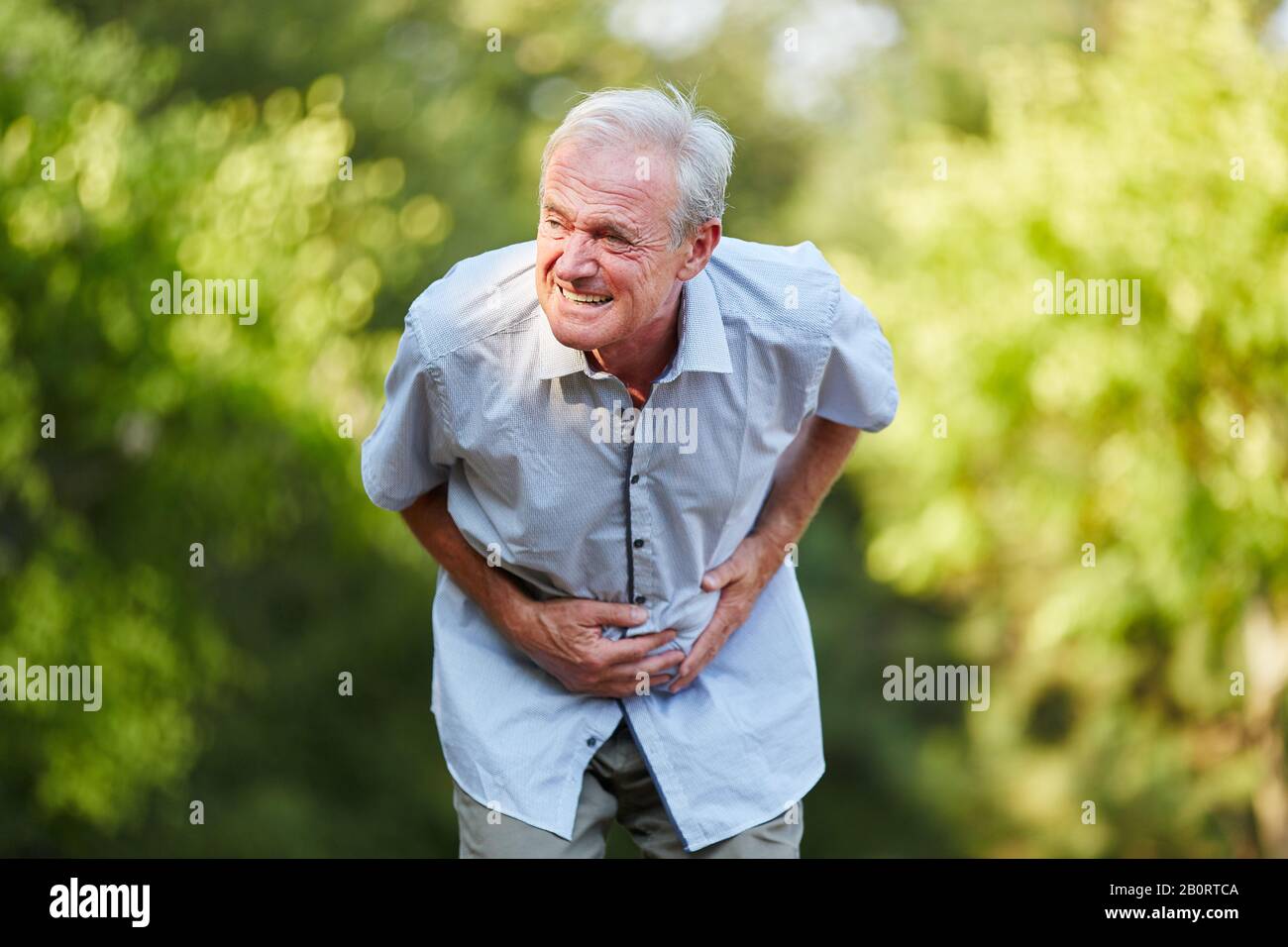 Alter Mann mit Magenschmerzen, der seinen Magen in der Natur hält Stockfoto