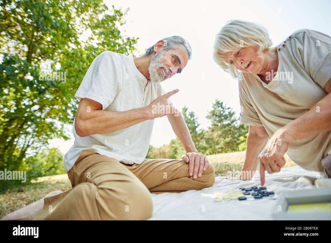 Ein Paar Senioren spielt im Sommer im Garten ein Brettspiel Stockfoto