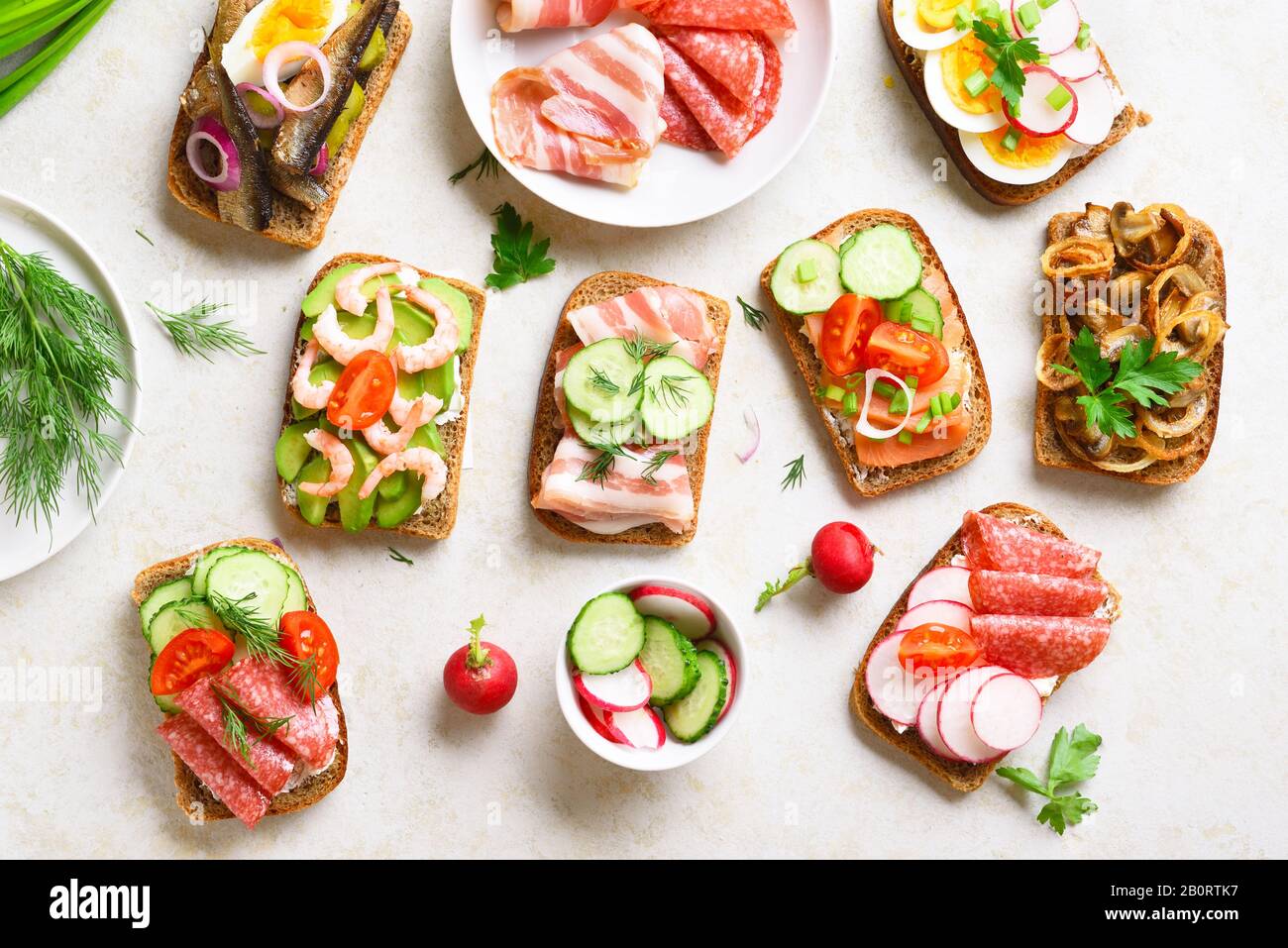 Verschiedene Sandwiches mit Fleisch, Gemüse und Seefahrt. Auswahl an offenen Sandwiches auf hellem Steingrund. Leckerer, gesunder Snack. Draufsicht, flach l. Stockfoto