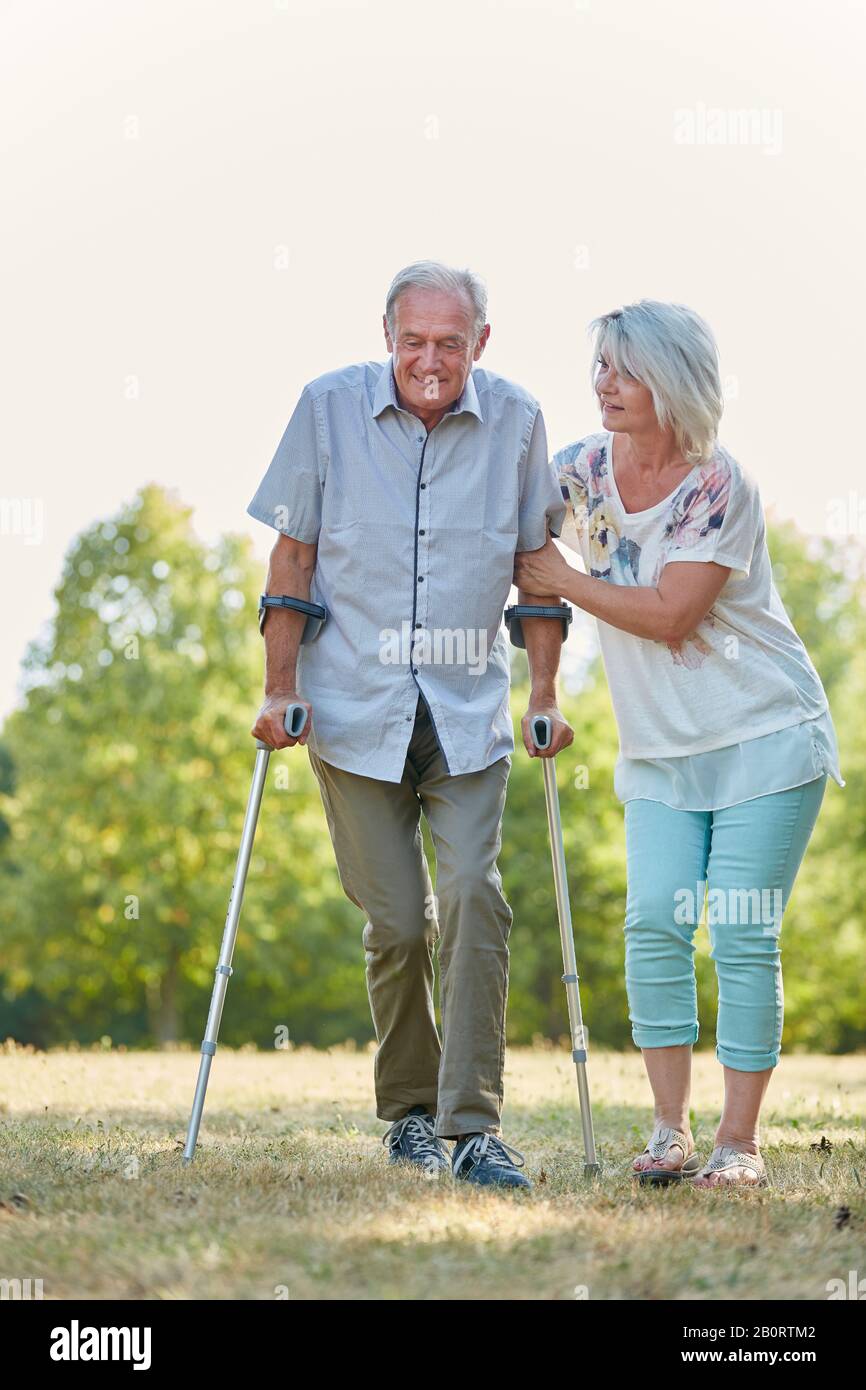 Der alte Mann geht mit Hilfe seiner Frau in der Natur mit einem Rohrstock spazieren Stockfoto