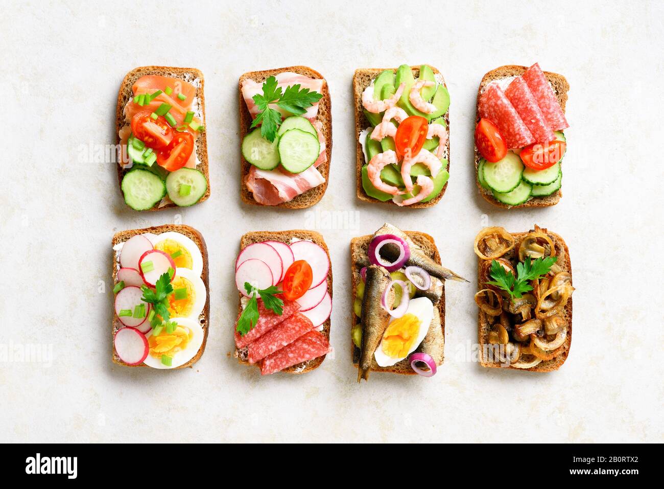 Verschiedene Sandwiches mit Fleisch, Gemüse und Seefahrt. Auswahl an offenen Sandwiches auf hellem Steingrund. Leckerer, gesunder Snack. Draufsicht, flach l. Stockfoto