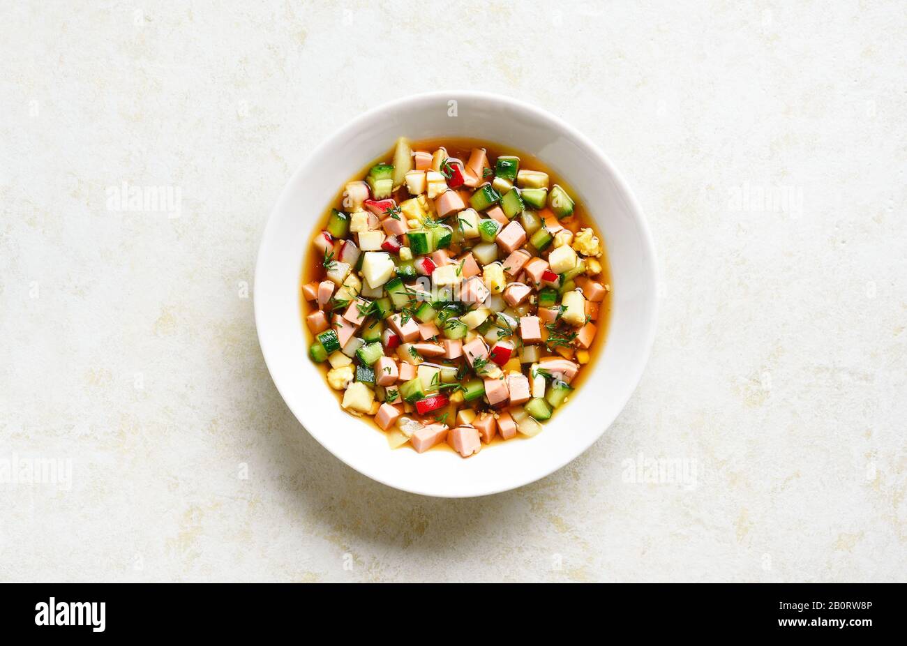 Okroschka-Suppe mit Wurst, Gemüse und Kvass über hellsteinem Hintergrund mit freiem Textraum. Traditionelle kalte russische Suppe. Draufsicht, flacher Lay Stockfoto