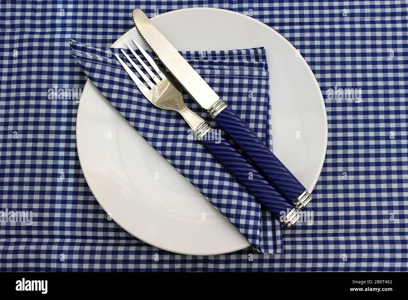 Eine weiße Platte mit Serviette und Messer und Gabel auf einem blauen Gingham Tischtuch Stockfoto
