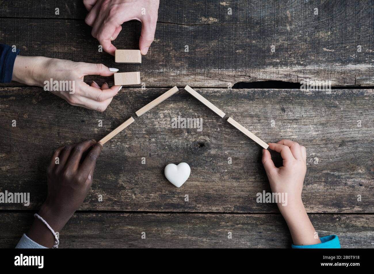 Gemischter Familienbau ein Haus aus Holzblöcken über rustikalem Holzhintergrund. Konzeptionelles Bild von Adoption und Familie. Stockfoto