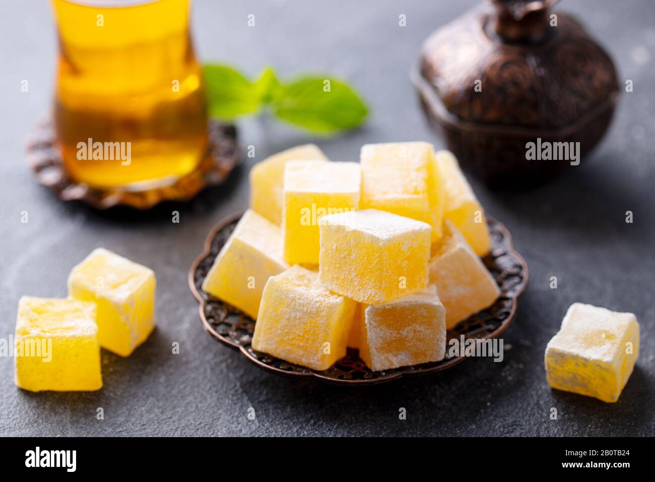 Türkische Freude auf einer Kupferplatte mit Glas Tee. Grauer Steinhintergrund. Nahaufnahme. Stockfoto