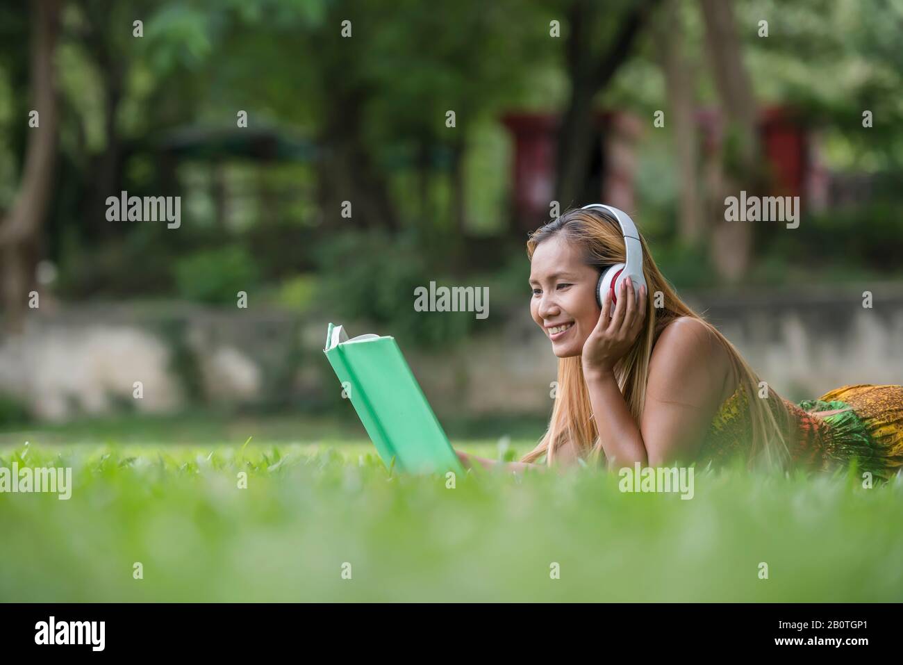 Asiatische Frau, die auf Kopfhörern Lieblingsmusik hört und ein Buch liest. Viel Spaß und Entspannung. Stockfoto