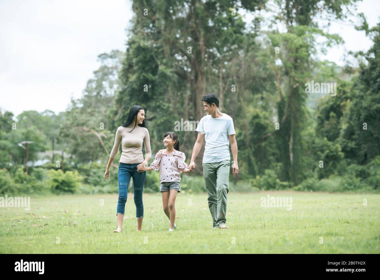 Glückliche Eltern und ihre Tochter, die im Park spazieren gehen, Glückliches Familienkonzept. Stockfoto