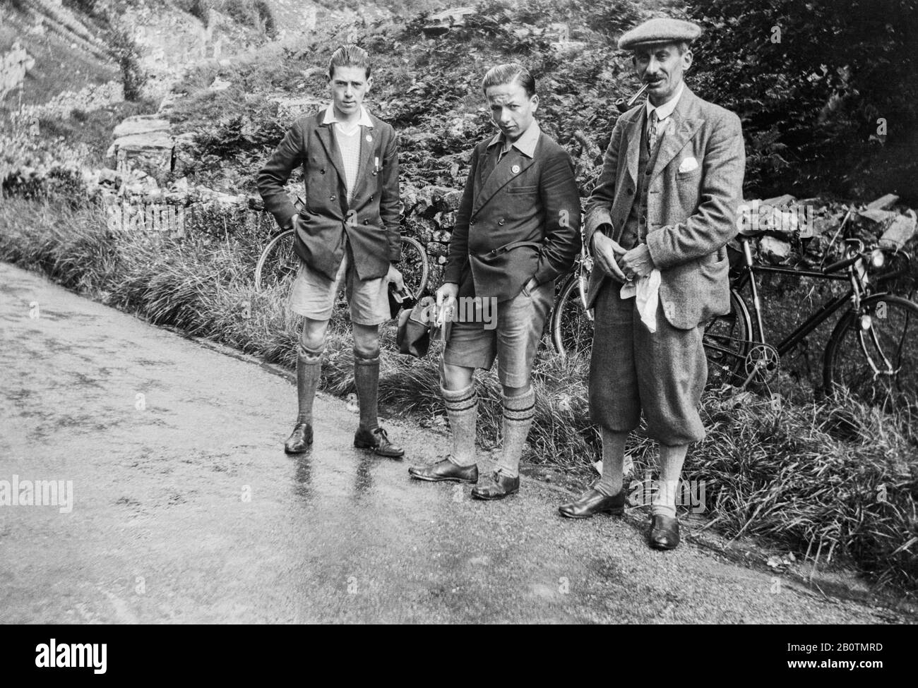 Drei Radfahrer stehen auf einer nassen Fahrbahn, die für ein Foto posiert. Zwei halten Cmeras, einer raucht ein Rohr. Derbyshire um 1920 Stockfoto