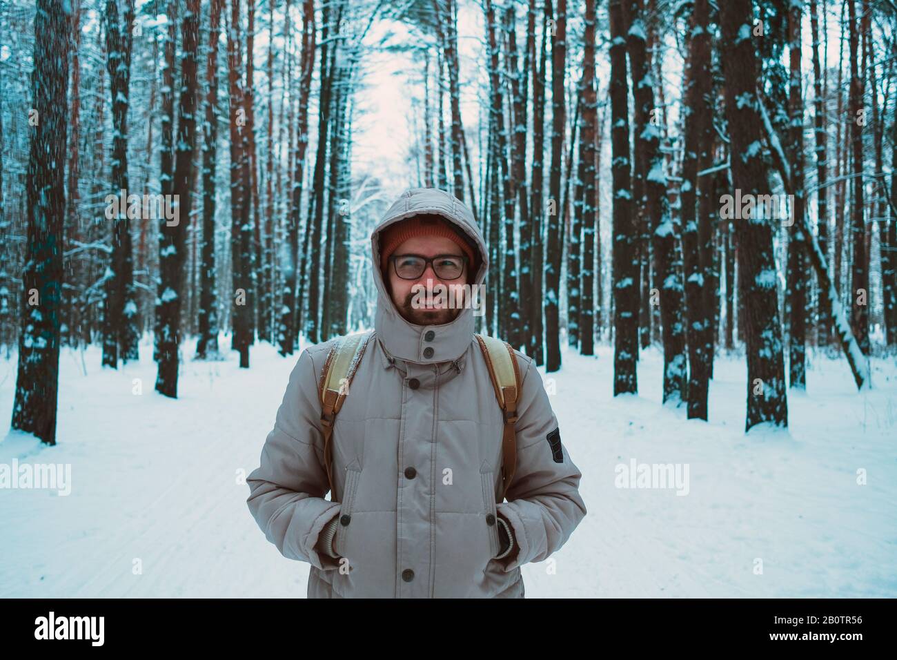 Ein bärtiger Mann in Hut und Rucksack steht mit dem Rücken im Winter in einem Nadelwald am Fluss. Das Konzept der Winterreise und Spaziergänge im Th Stockfoto