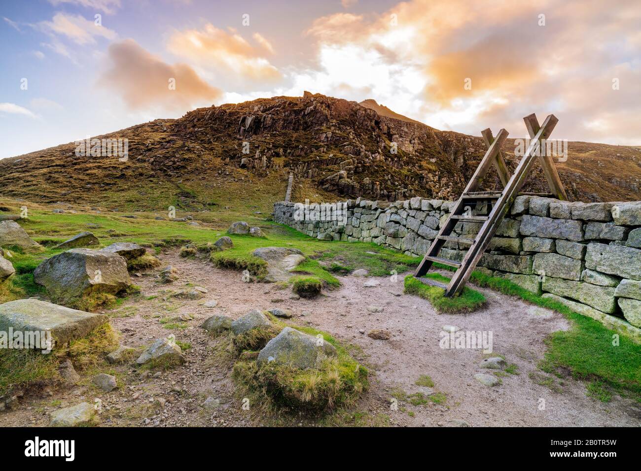 Mourn Wall mit Leiter auf der Hares Gap, die den Berg Slieve Bearnagh mit Sonnenuntergang zu goldener Stunde beaufsichtigt. Mourne Mountains Range in Nordirland Stockfoto