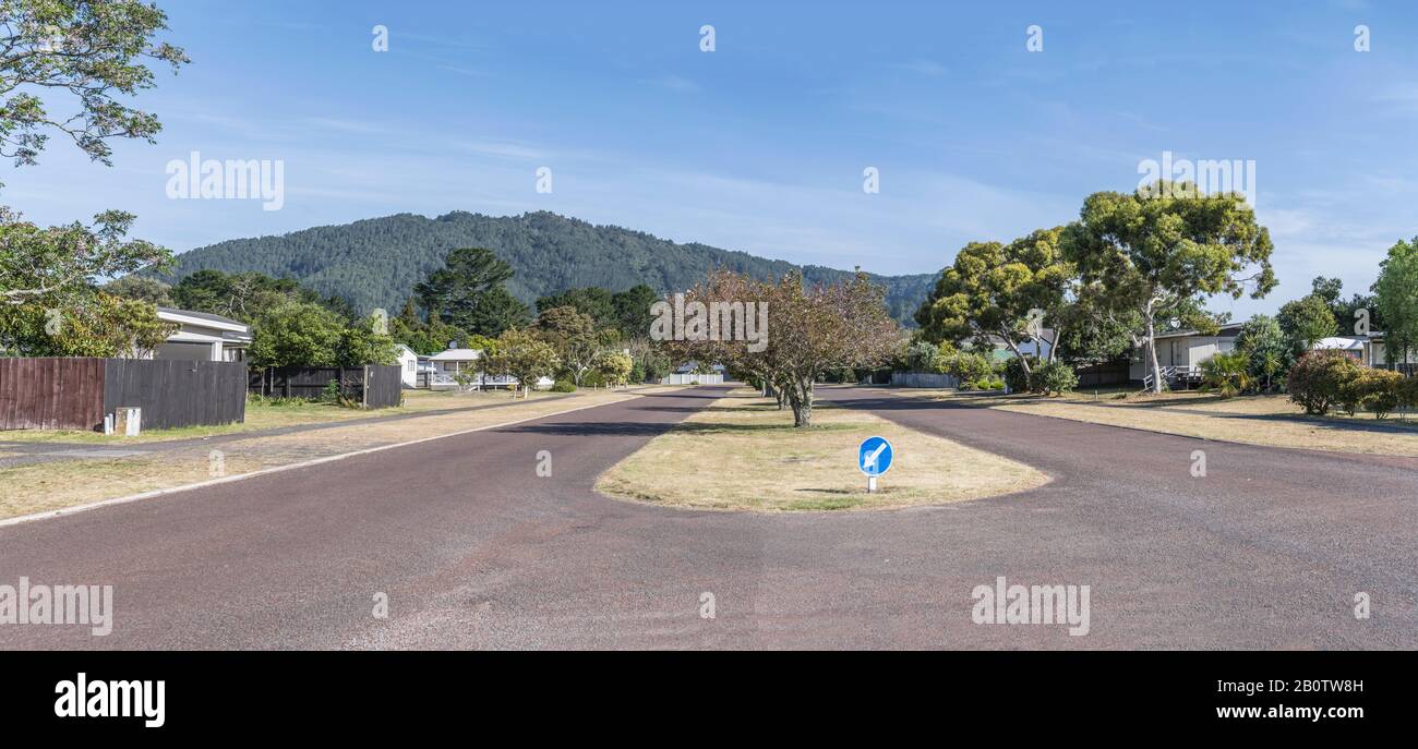 Stadtbild eines grünen toruristischen Dorfes mit einer großen doppelspurigen, von Bäumen gesäumten Straße, in hellem Spätfrühling hell auf Pauanui, Coromandel, North Island, N geschossen Stockfoto