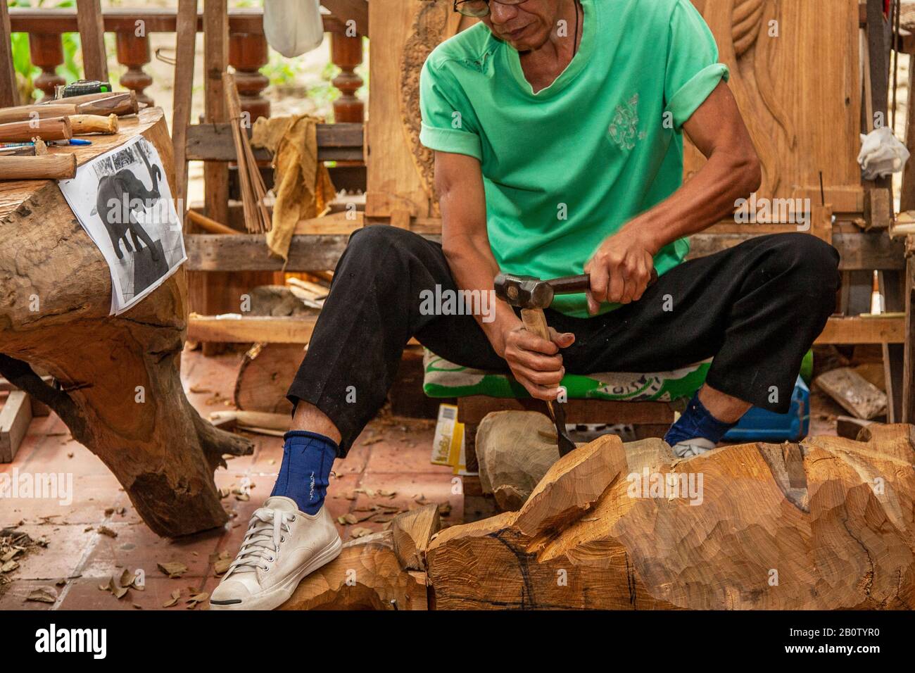 Asiatische handgefertigte Tische und Stühle in Möbelwerkstatt: Eine Touristenattraktion, die einzigartige, wiederverwendete Holzschnitzereien herstellt. Handgemeißelte Stücke, feine Handwerkskunst mit Tier- und Landschaftskunst für den Export, in Thailand: Eine Touristenattraktion, die einzigartige, wiederaufbereitete Holzschnitzel herstellt. Handgemeißelte Stücke, feine Handwerkskunst mit Tier- und Landschaftskunst für den Export nach Thailand, Großbritannien Stockfoto