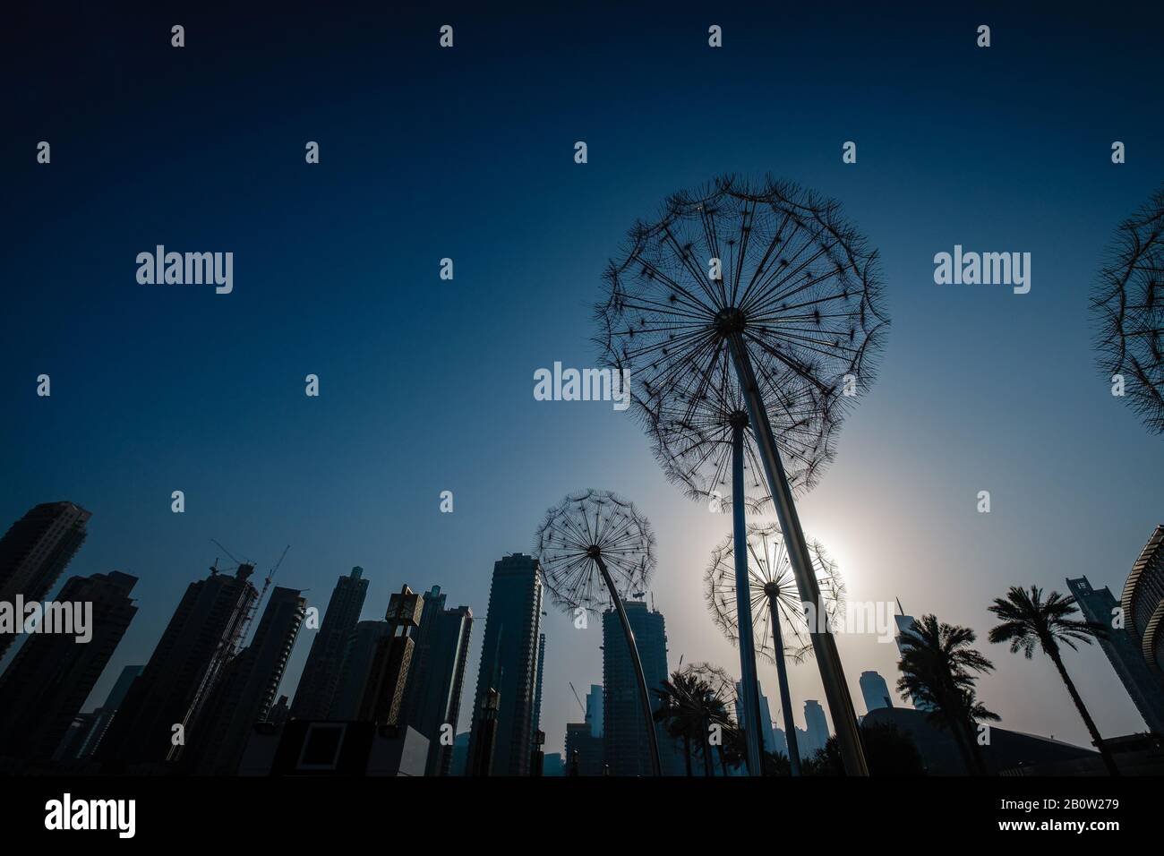 Riesige Metall-Löwenzahn-Skulptur im A-Park in Dubai, Silhouette von Löwenzahn und Wolkenkratzern gegen einen strahlenden Himmel bei Sonnenuntergang Stockfoto