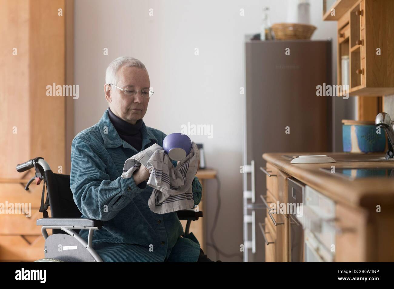Seniorin sitzt im Rollstuhl in ihrer Küche, dryng nach oben. Stockfoto