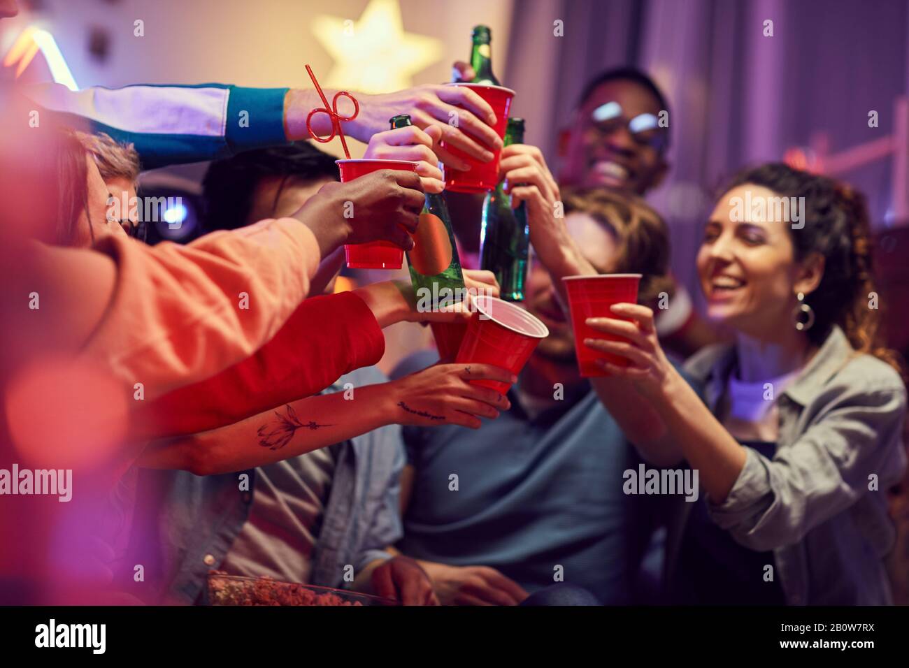 Nahaufnahme junger glücklicher Freunde, die während einer lustigen Party Bier trinken und damit toasten Stockfoto