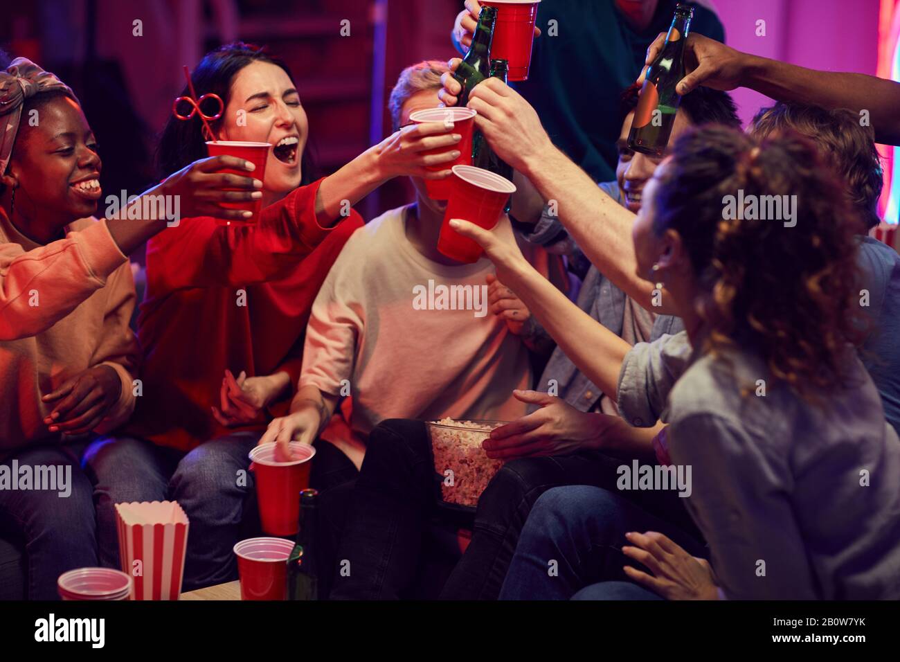 Eine Gruppe glücklicher Freunde, die mit Alkoholgetränken toben, während sie auf dem Sofa sitzen und ihr Treffen feiern Stockfoto