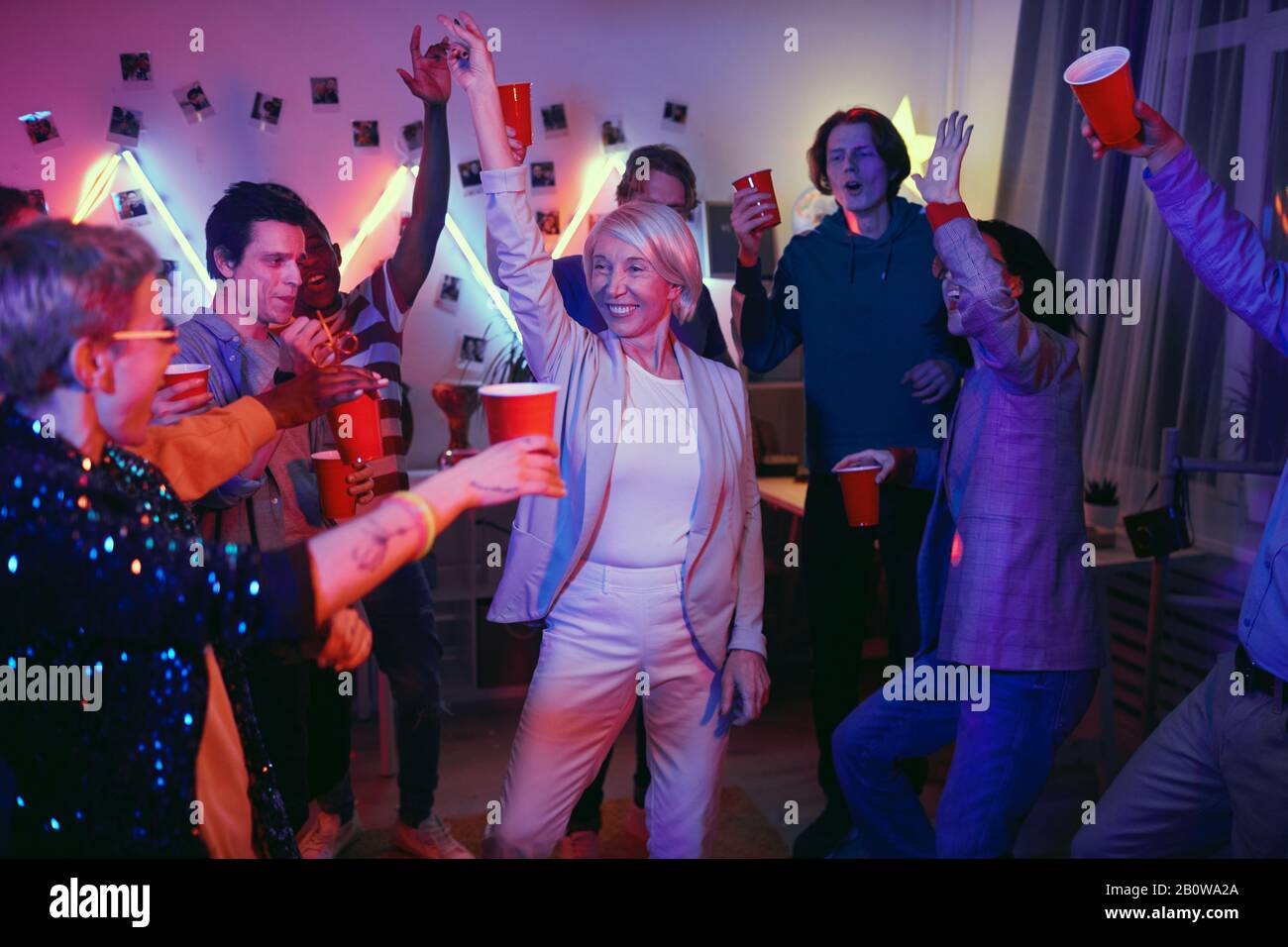Lächelnde, reife Frau tanzt und hat Spaß an der Party unter Jugendlichen Stockfoto
