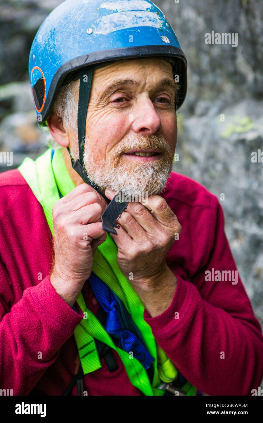 Ein reifer Bergsteiger, der seinen Helm aufsetzt und für einen Aufstieg vorbereitet. Stockfoto