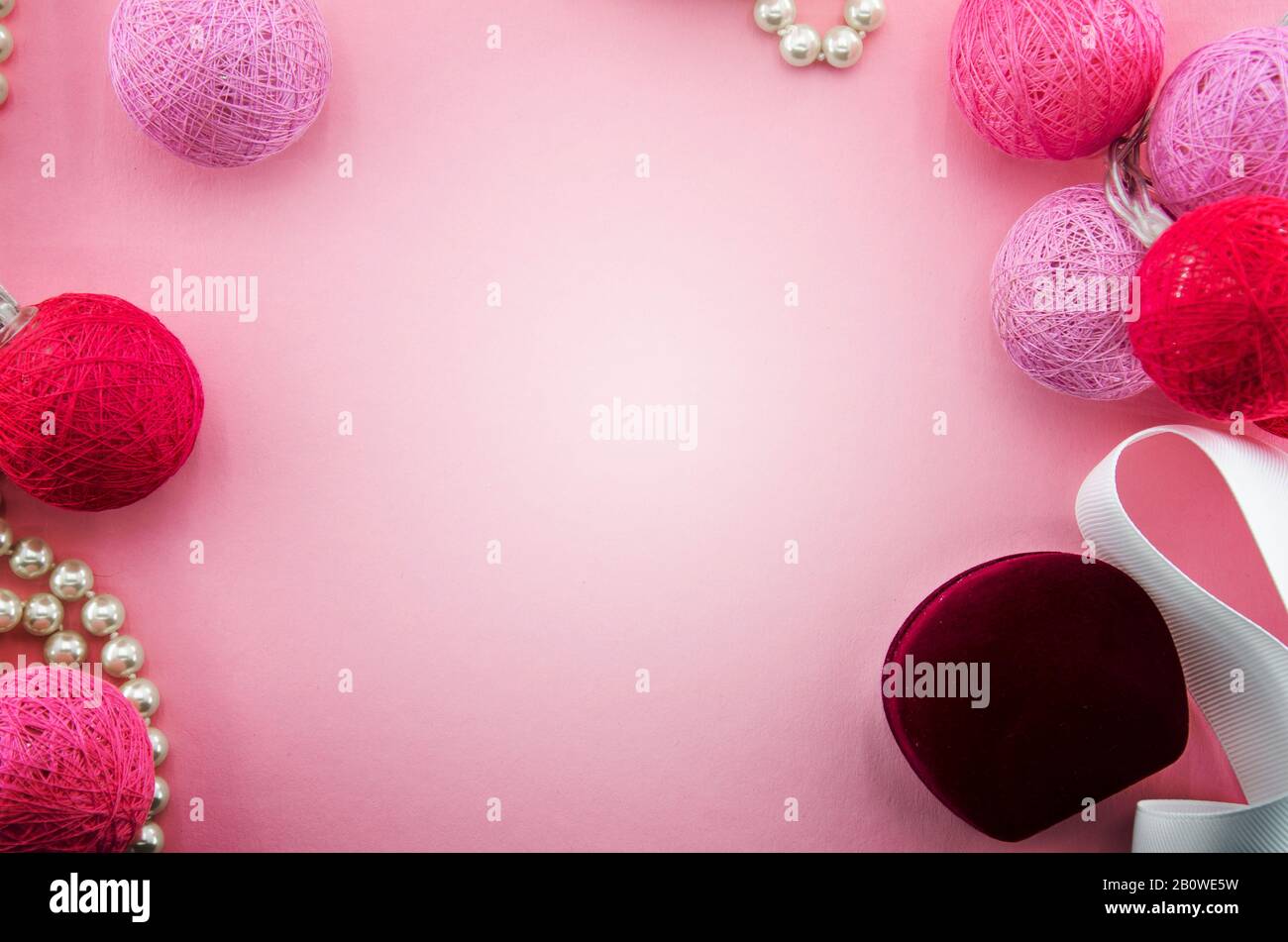 Rosafarbener Hintergrund mit rosafarbenem und rotem Garn oder Fäden Kugeln garland, weißes Band, Schmuckkiste, Perlenkette. Beleuchtung von Baumwoll-Fadenkugeln. Valentines Stockfoto