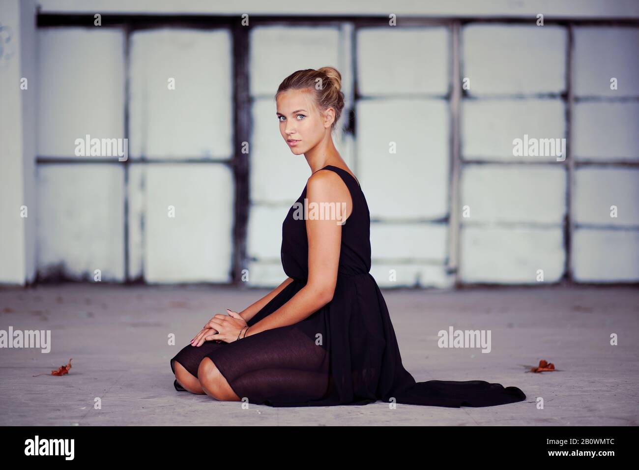 Junge Frau in schwarzem Kleid kniet auf dem Boden Stockfoto