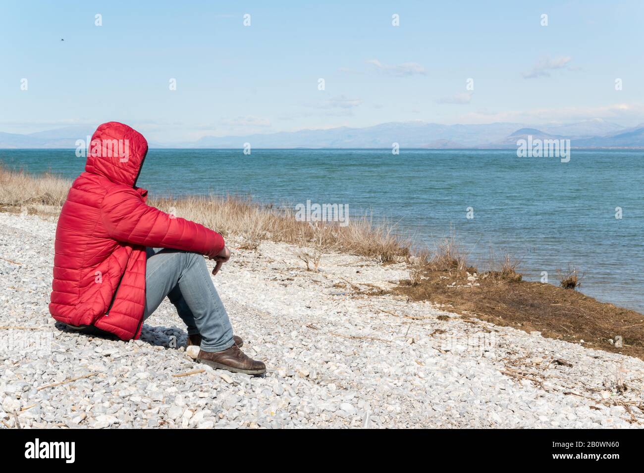 Einsamer Mann, der auf dem Seeufer sitzt und die Natur bewundert. Unerkennbare Person, Wanderlust Stockfoto