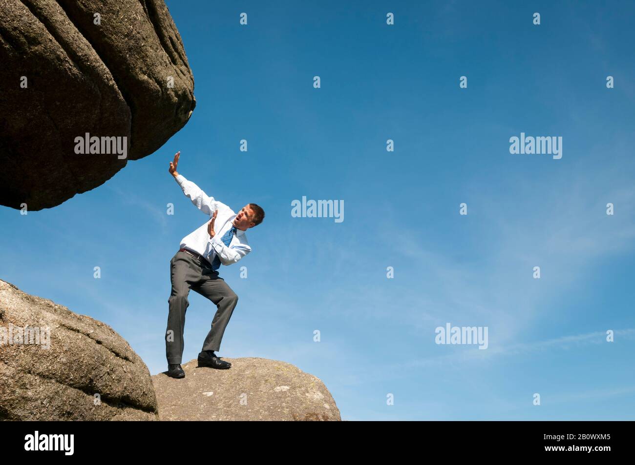 Der kleine Geschäftsmann, der seine Hände in Richtung eines massiven Felsboulders hält, der über ihn hinabrollt Stockfoto