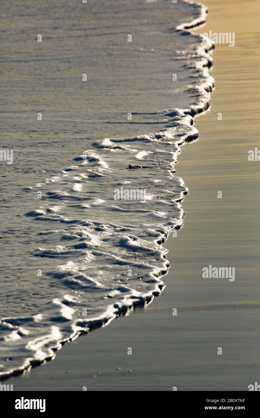 Wasser und Schaum, die bei Ebbe über Sand fegen. Dorset England GB Stockfoto