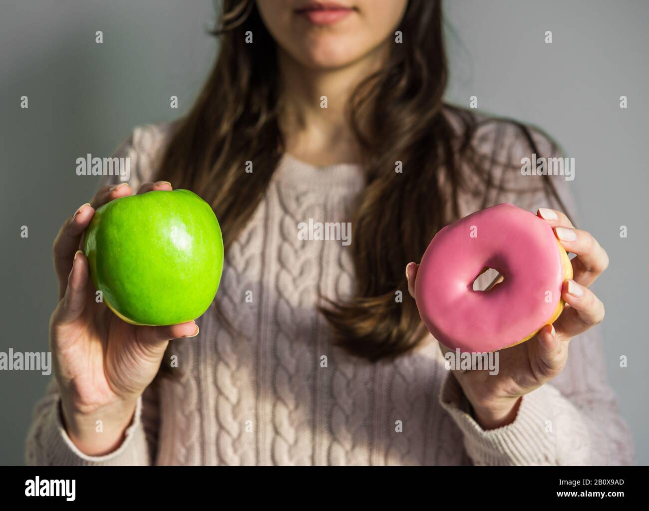 Frau, die einen Donut und grünen apfel hält. Konzept von gesunden und ungesunden Lebensmitteln. Stockfoto