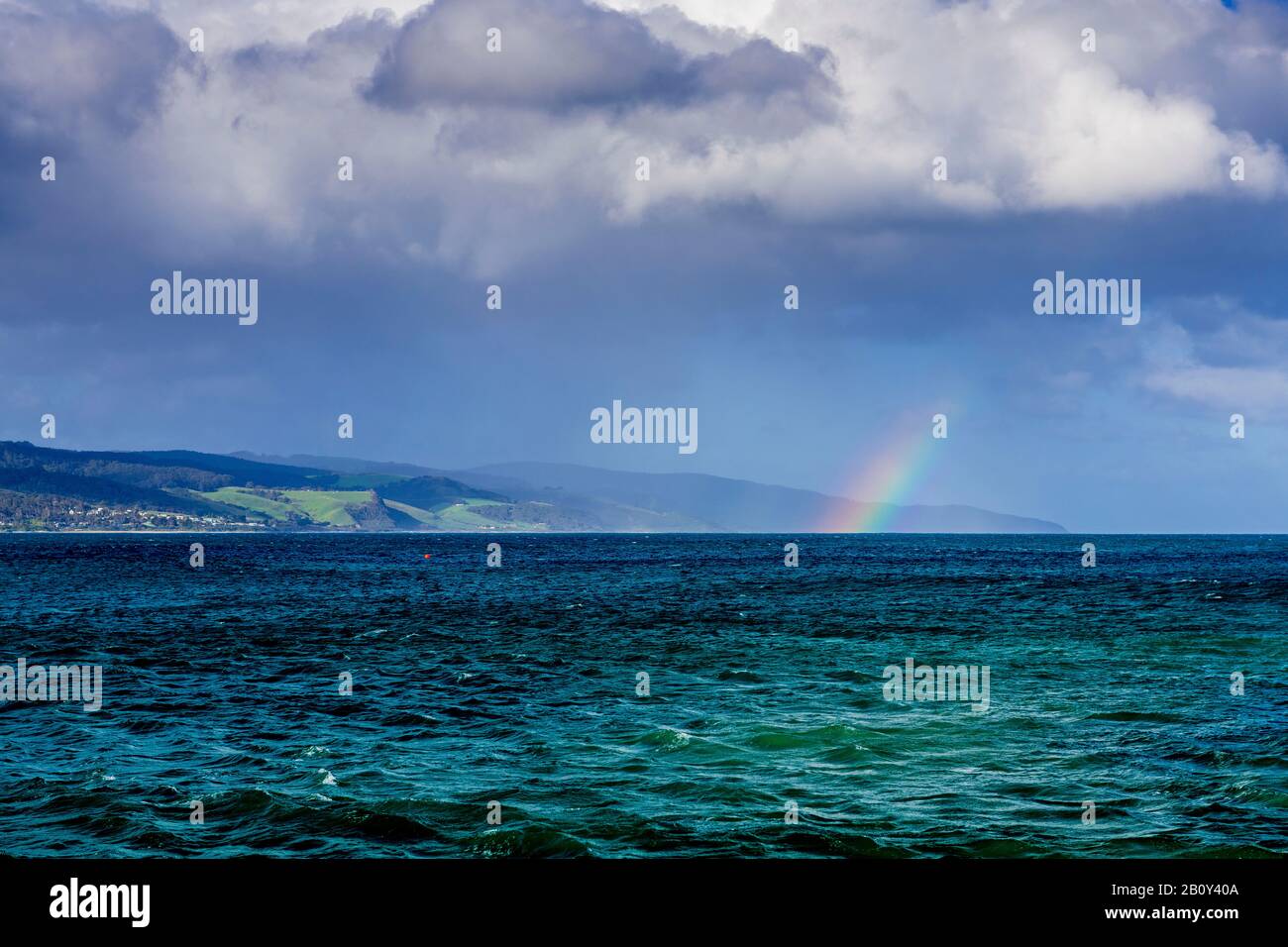 Apollo Bay mit Regen, der sich nähert und einen kleinen Regenbogen über dem Wasser bildet. Victoria, Australien Stockfoto