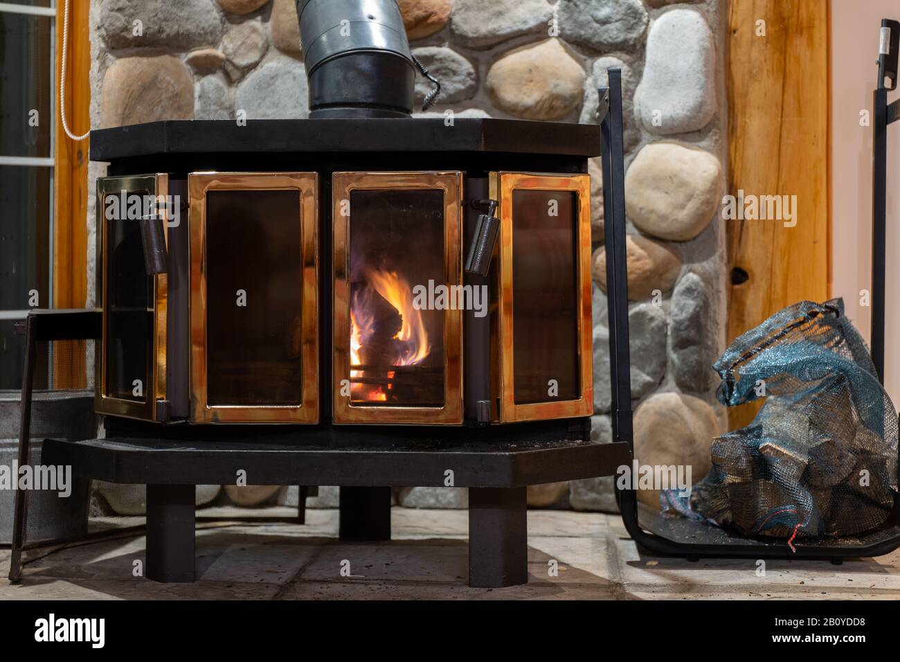 Kaminofen aus Holz mit Metallgehäuse und Glastür im Haus mit gemütlichem Interieur. Stockfoto