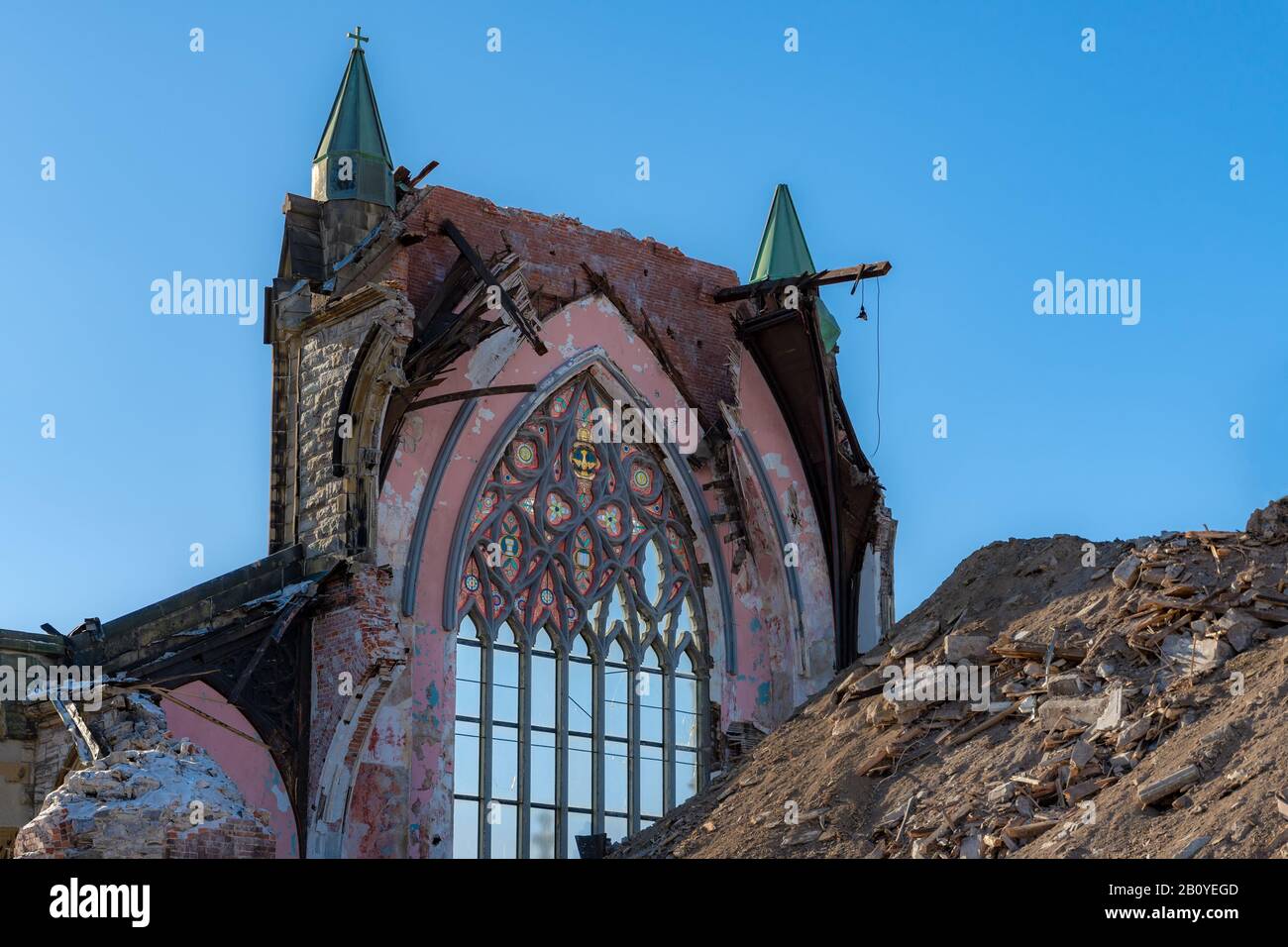 Die Ruinen einer großen gotischen Kirche. Es bleibt nur noch eine Wand, es hat oben ein großes Fenster mit Glasflecken. Großer Trümmerhaufen davor. Sonnig d Stockfoto